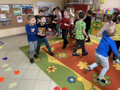 Dzieci chodzą po sali przedszkolnej i naśladują ruchem i głosem zachowanie dinozaurów