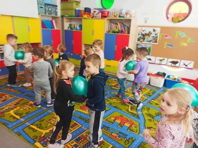 Dzieci stoją naprzeciwko siebie i trzymają pomiędzy sobą nadmuchane balony jako olbrzymie jaja dinozaurów.