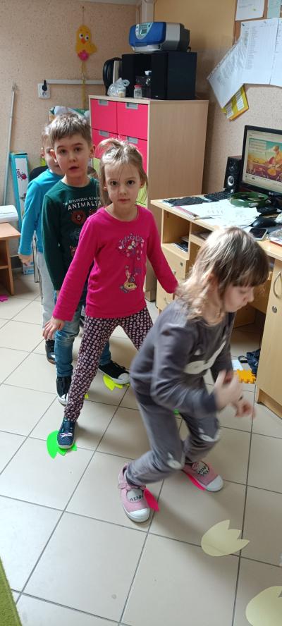 Dzieci z grupy Skrzaty wykonują ćwiczenia. Na podłodze umieszczone są ślady dinozaurów po których każde dziecko skacze