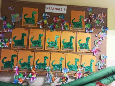 Na tablicy korkowej w szatni przedszkolnej powieszone są prace dzieci  z grupy ,,Krasnale kolorowe sylwetki dinozaurów.