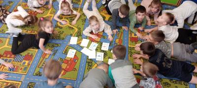 Przedszkolaki bawią się w dinusiową gimnastykę z kartami dinozaurów. Wykonują poszczególne ćwiczenia. Nie wszystkie kar
