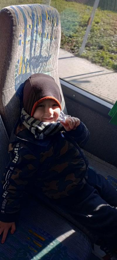 Chłopiec na fotelu w autobusie, uśmiecha sie do fotografującej osoby i wskazuje kciukiem do góry.