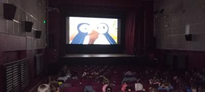 Dzieci siedzące i oglądające bakę w kinie. Na ekranie widoczne dwa maskonury.