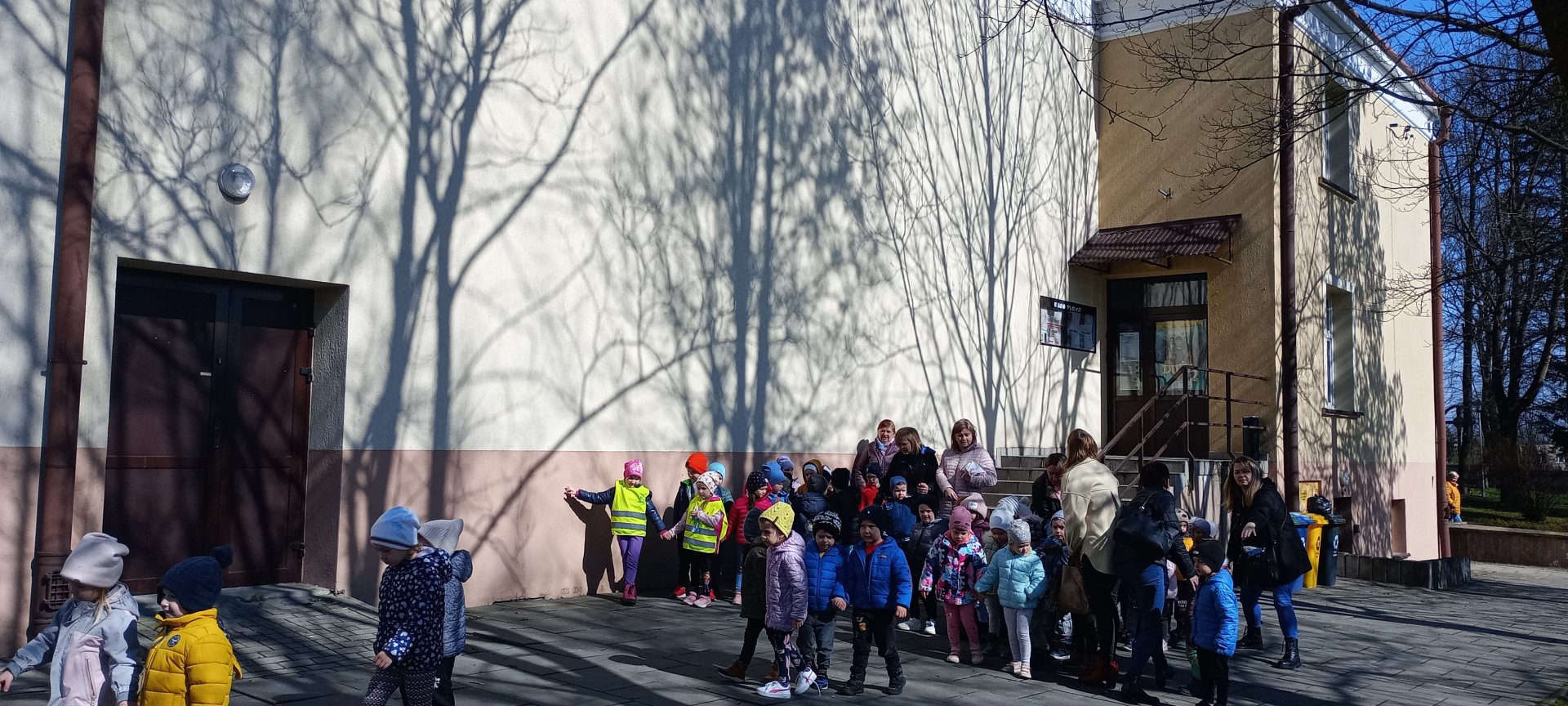Grupy przedszkolne przed budynkiem kina Farys. Przedszkolaki ustawione parami oraz grupami ze swoimi wychowawcami.